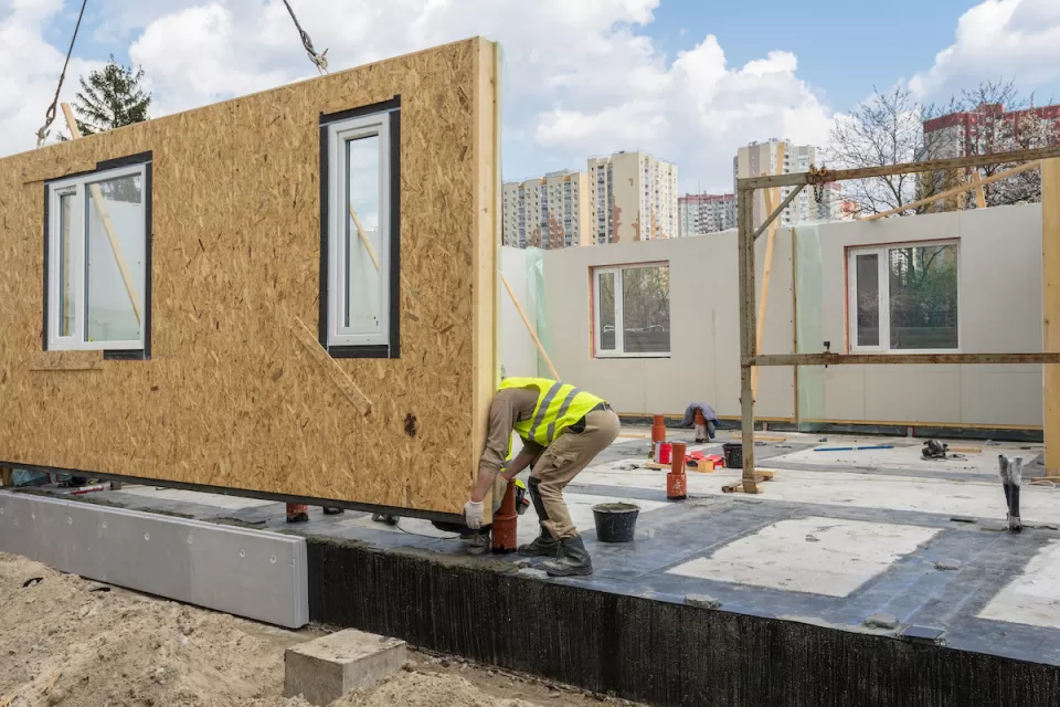 Worker in yellow construction vest working on modular home under construction.